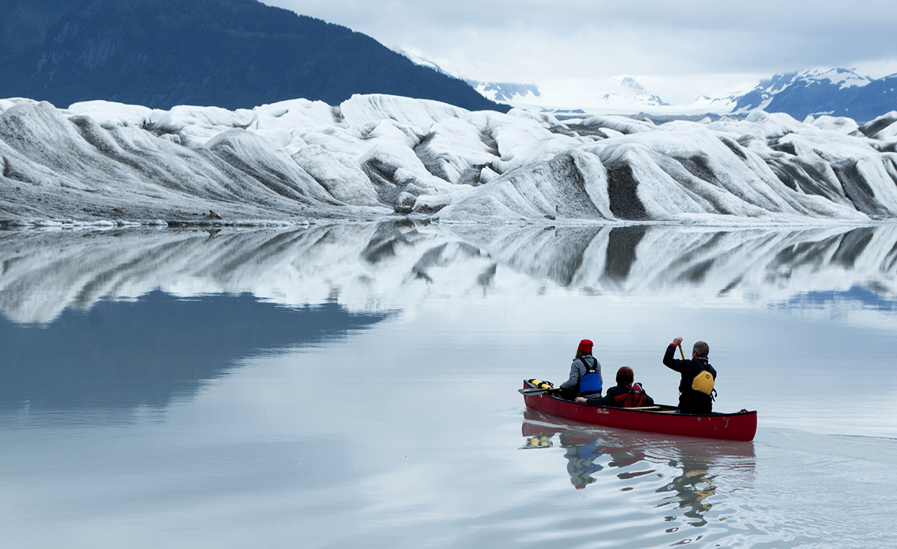 A student and faculty with the University of Oregon School of Journalism and Communication's Science and Memory program canoe into the shadow of a glacier in pursuit of a story.